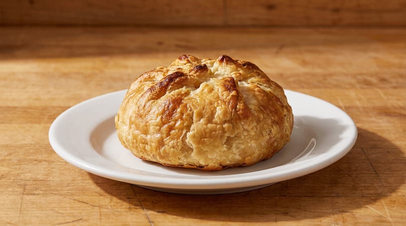 Golden baked puff pastry on a white plate, resting on a rustic wooden surface.
